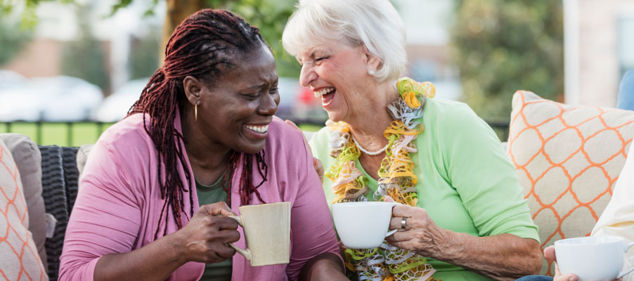 Two women smiling on a bench while enjoying a hot beverage.