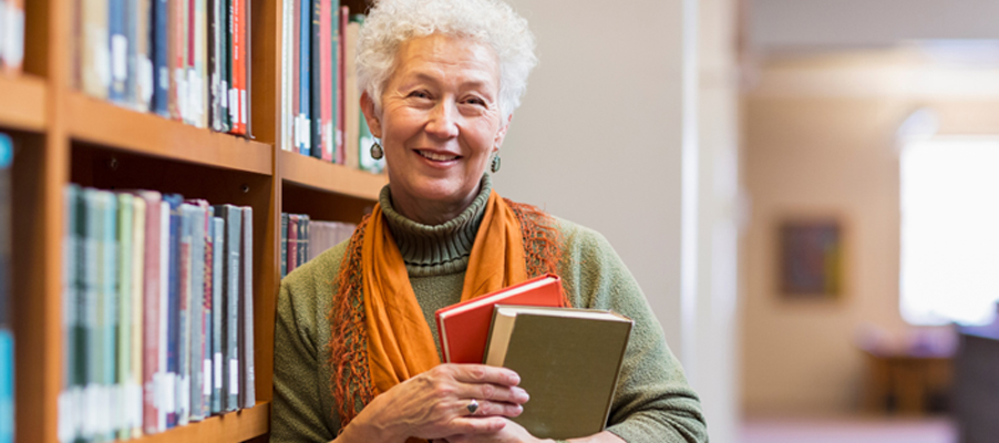 Older woman smiling while holding books in a library.