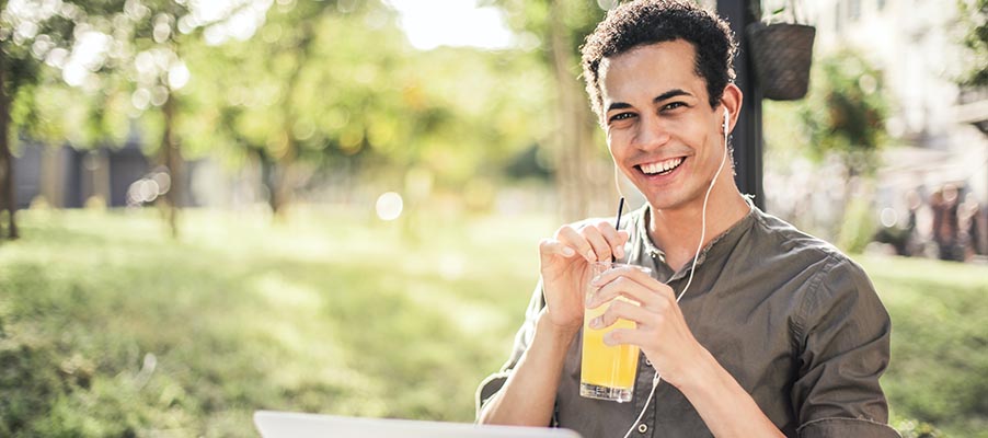 A younger person outside wearing headphones and holding a drink.